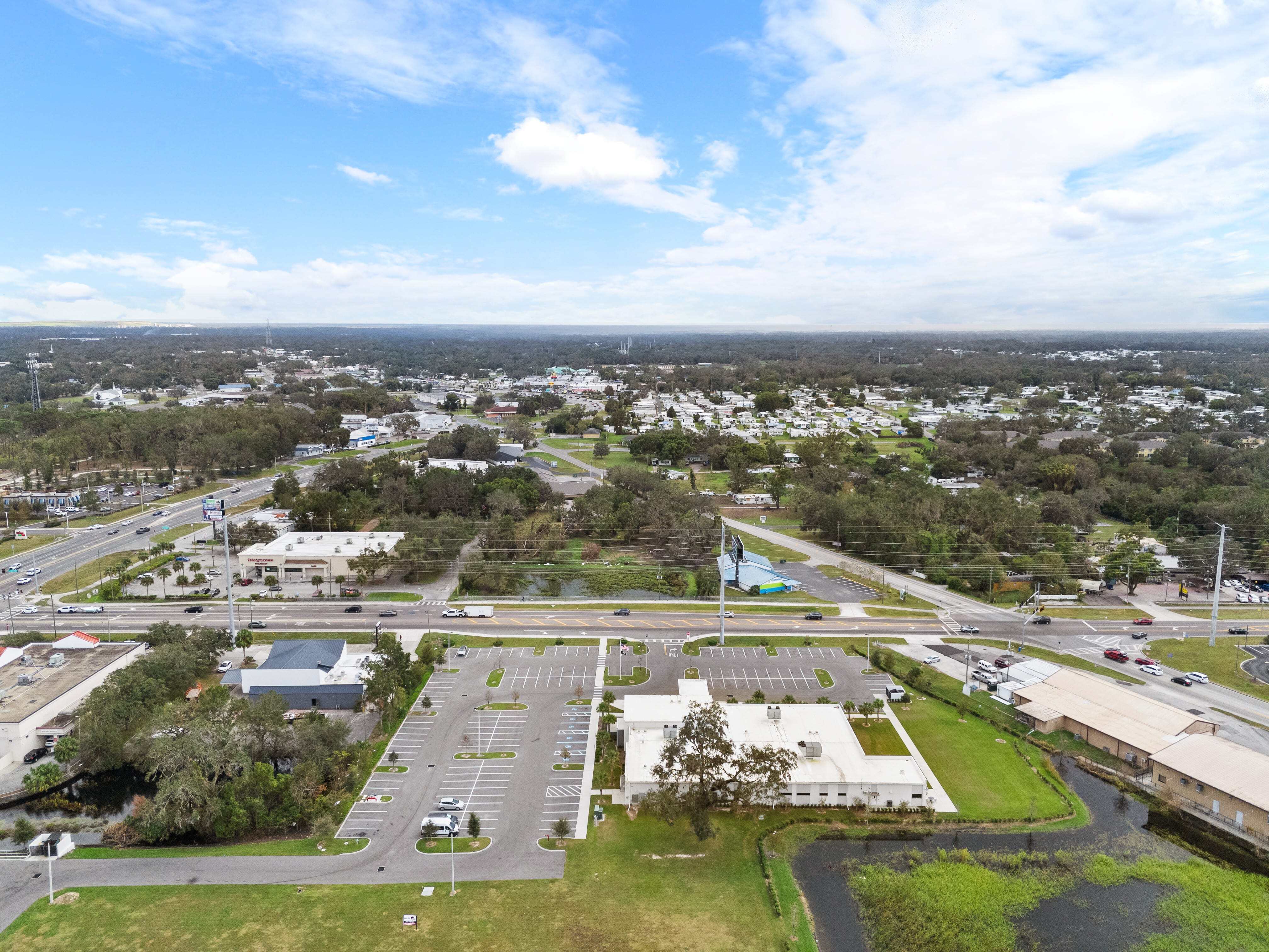 Zoomed-out drone aerial of Zephyrhills VA Clinic showing clinic footprint, rear lot, and nearby commercial strip