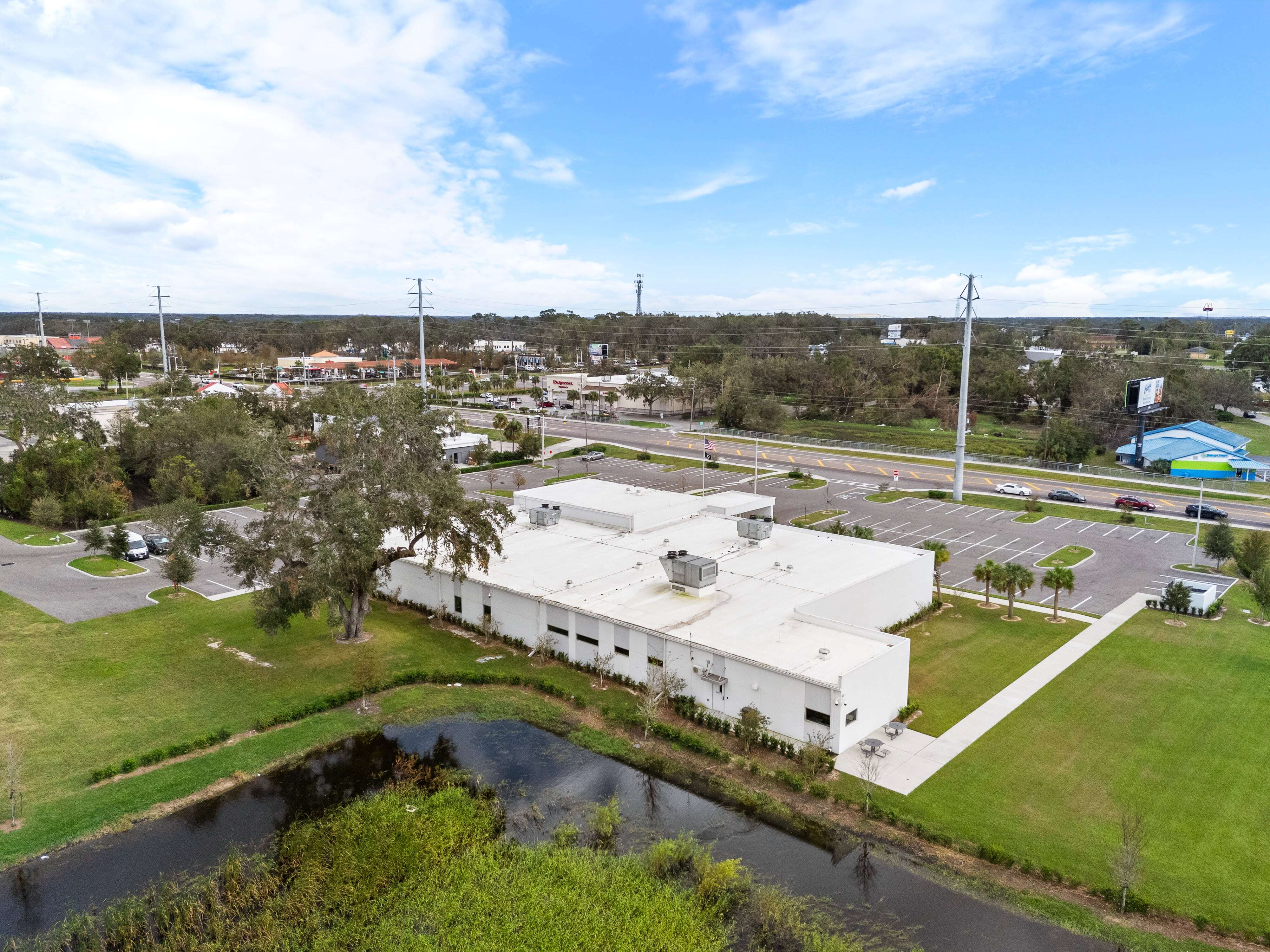 Angled drone shot of rear and side of Zephyrhills VA Clinic showing landscaping, roof units, and adjacent pond