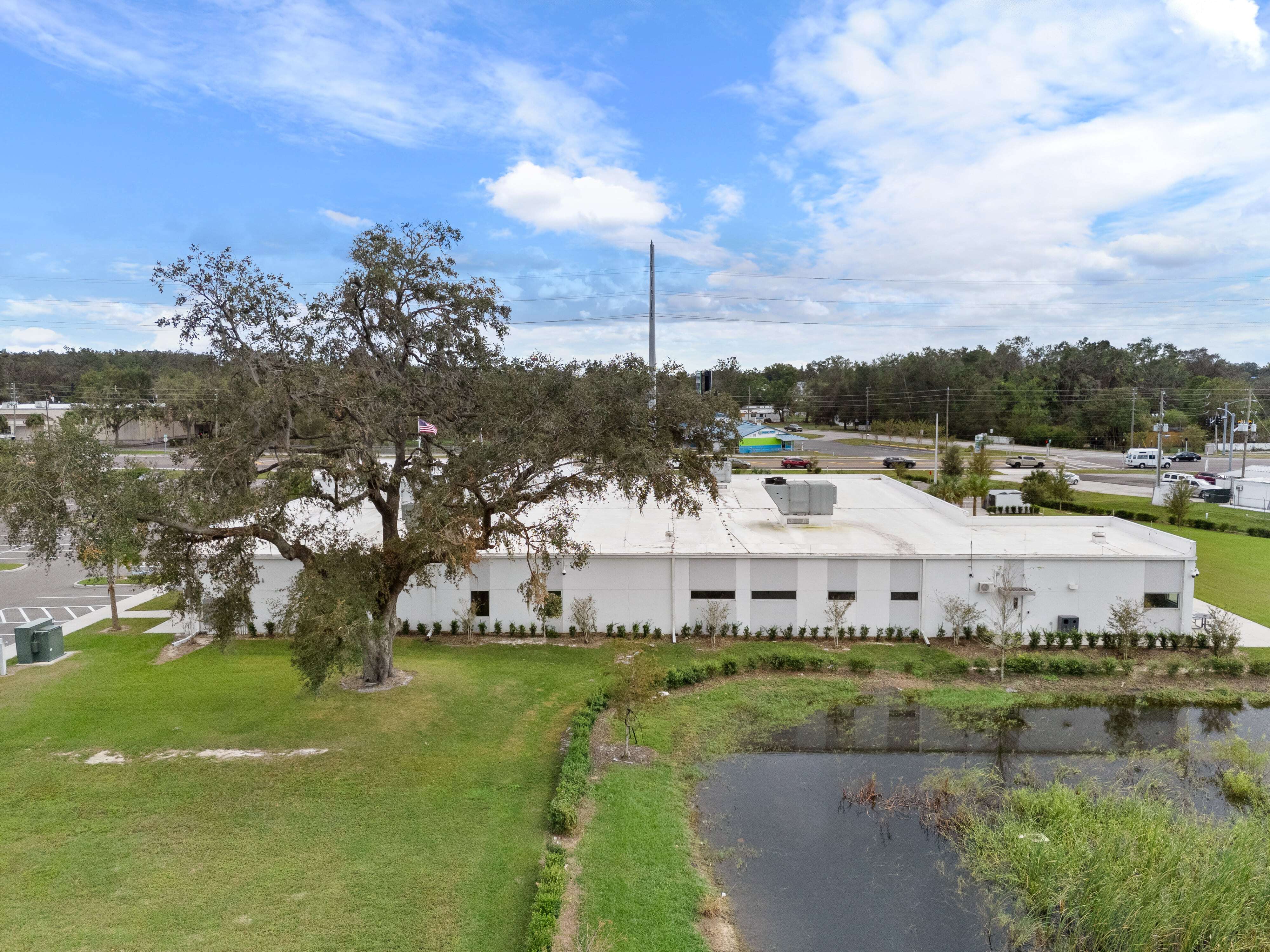 Straight-on view of the rear side of Zephyrhills VA Clinic showing roofline, tree, and pond in foreground
